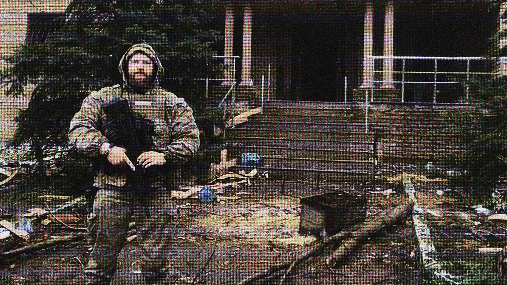 Боєць у бронежилеті стоїть біля зруйнованої будівлі з автоматом